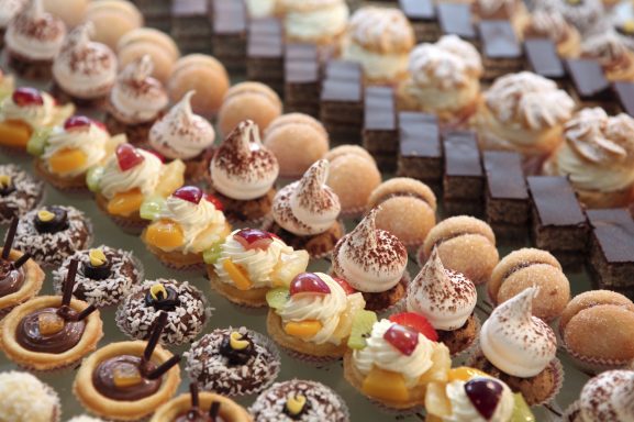 Bunte Auswahl an kleinen Gebäckstücken, Törtchen und Desserts auf einem Tablett.