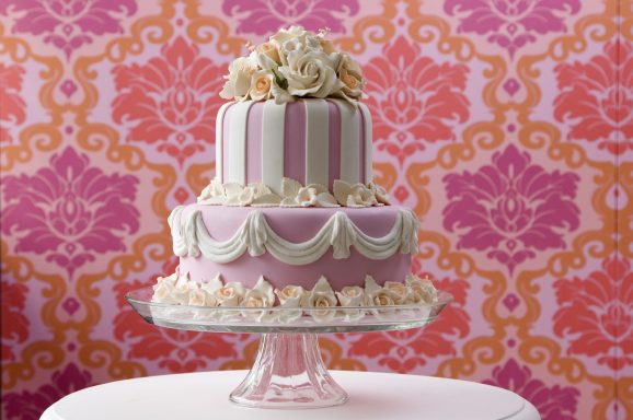 Elegante zweistufige Torte mit rosa und weißen Zierleisten und einer Blumendekoration.