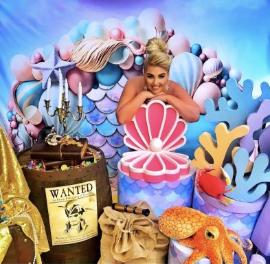 Frau im Meerjungfrauenkostüm mit Dekorationen, Muscheln und einem Oktopus.