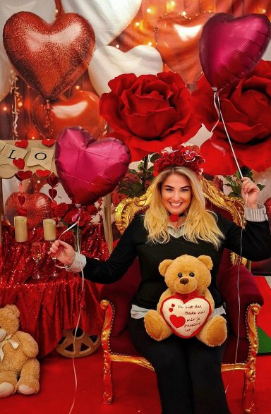 Frau in rotem Raum mit Herzballons und einem Teddy, umgeben von Rosen.