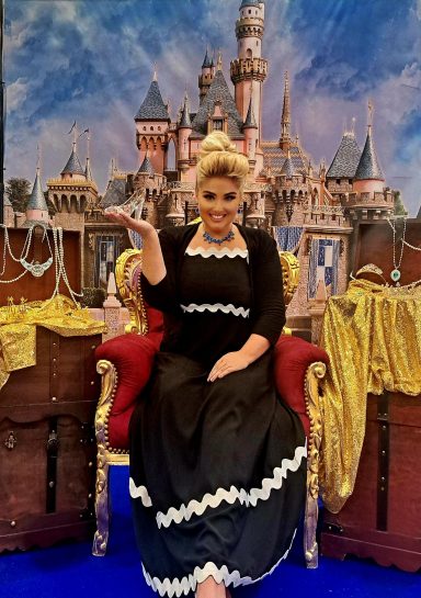 Frau in schwarzem Kleid sitzend auf Thron vor einem Märchenschloss.