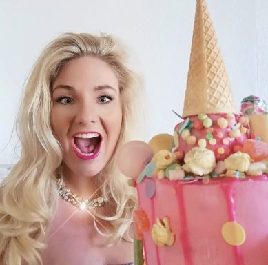 Blonde Frau mit offenem Mund und einem bunten, mit Süßigkeiten dekorierten Kuchen.